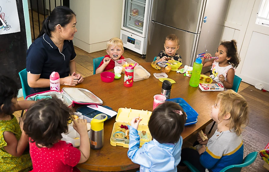 An educator sitting at a low table with a group of children during an indoor activity