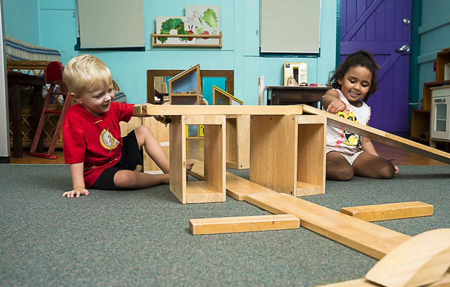 A boy and a girl playing side by side with wooden blocks on the floor