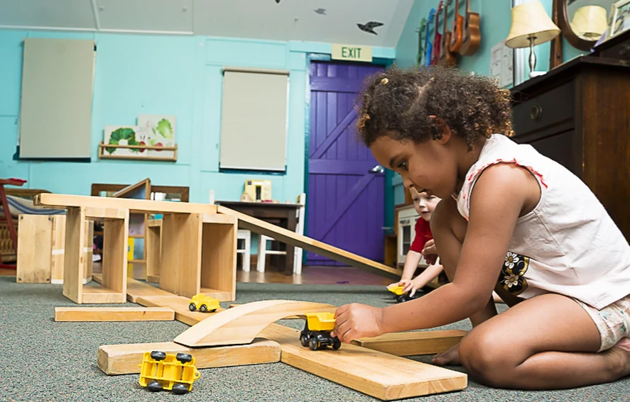 A child kneeling on the floor, absorbed in building with wooden blocks and toy trucks