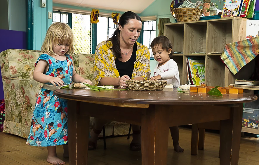 An educator working one-on-one with two children at a wooden table