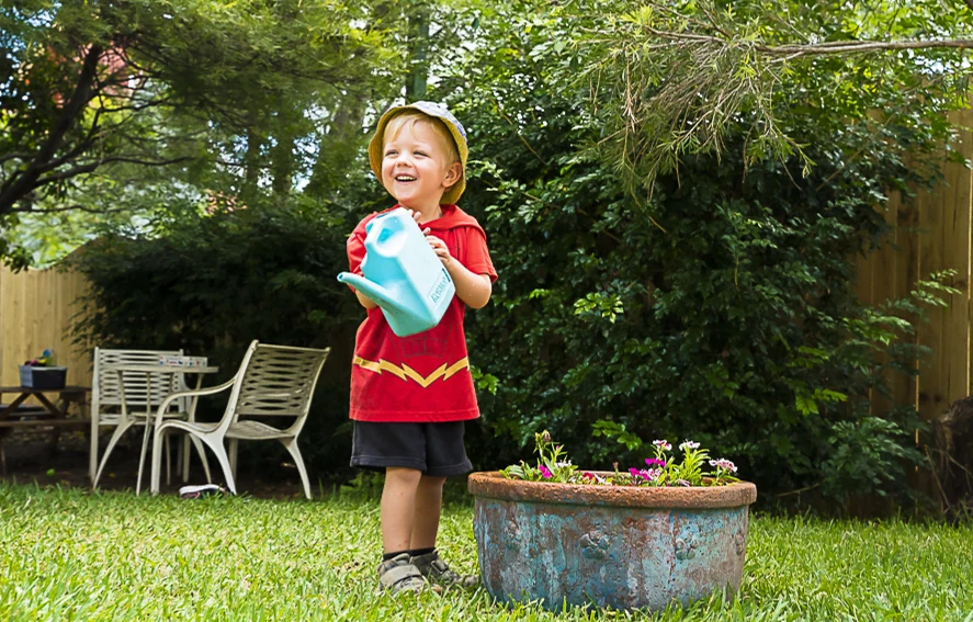 A young girl in a red dress holding a watering can in the garden