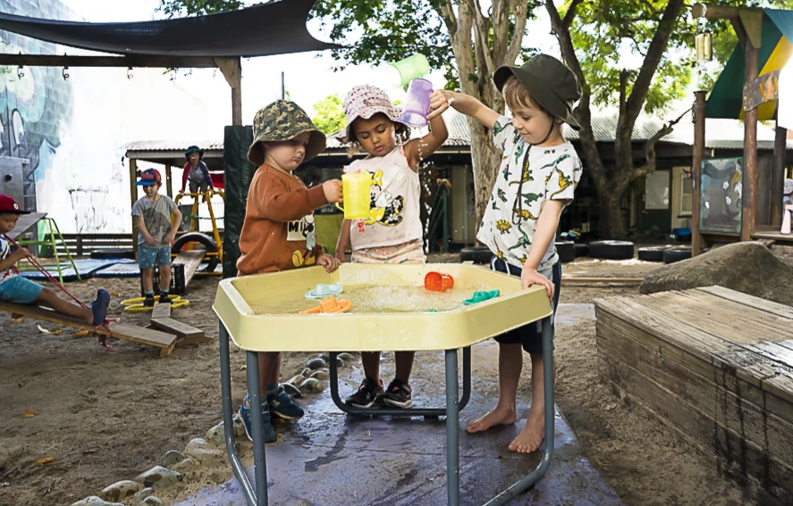 Children gathered around a table in the sandpit, cooking with pots and pans
