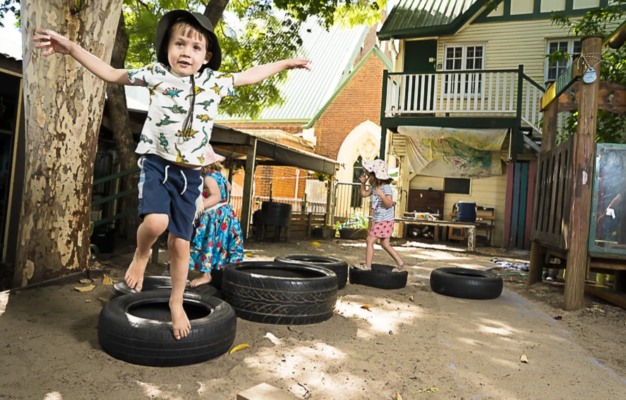 A boy standing tall with arms outstretched on a tyre, smiling
