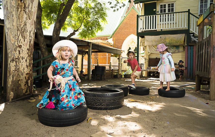 A girl in a floral dress climbing onto a tyre in the yard