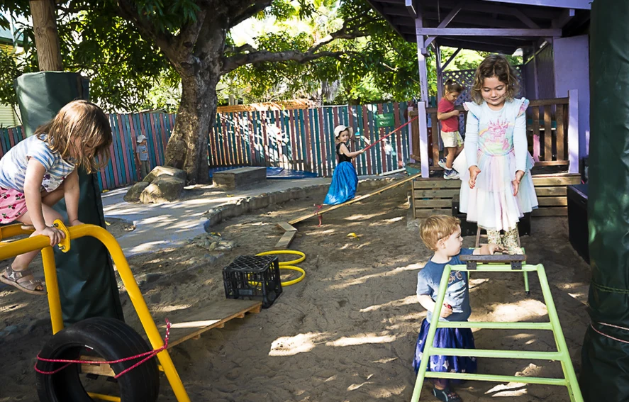 A child stepping across a low balance ladder in the shaded outdoor play area