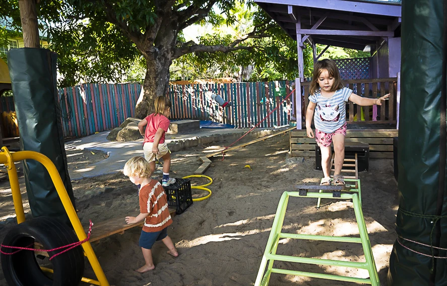 An educator steadying a child as they climb a small ladder in the playground